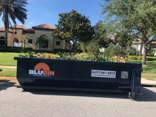 BluBin dumpster filled with yard debris on a residential street